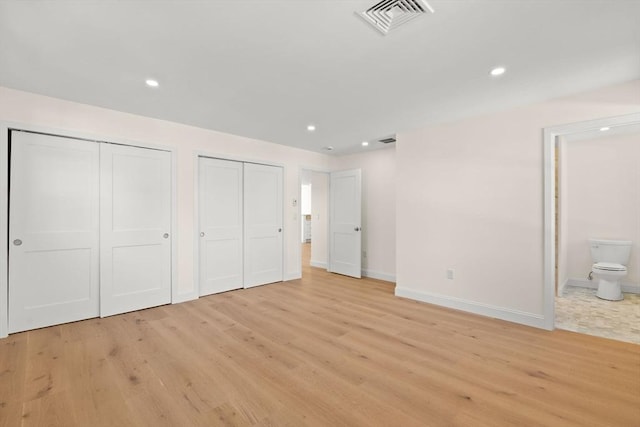 unfurnished bedroom with two closets, light wood-style flooring, baseboards, recessed lighting, and connected bathroom