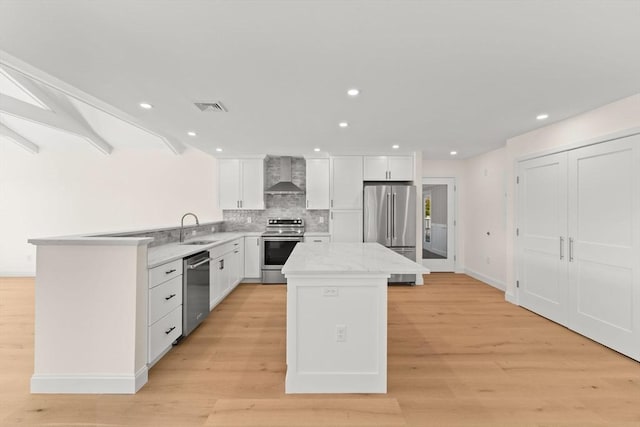kitchen with appliances with stainless steel finishes, wall chimney range hood, a sink, a kitchen island, and white cabinets
