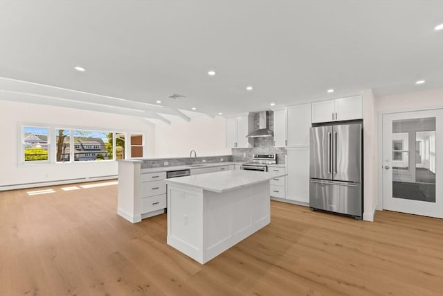 kitchen with stainless steel appliances, wall chimney range hood, a sink, light wood-style flooring, and a center island