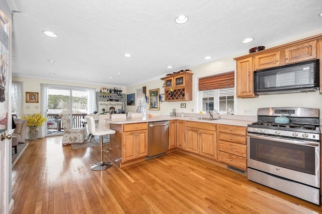 kitchen with a peninsula, a sink, ornamental molding, light countertops, and stainless steel appliances