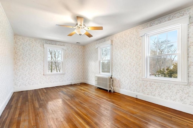 spare room featuring ceiling fan, a wealth of natural light, radiator heating unit, and hardwood / wood-style flooring