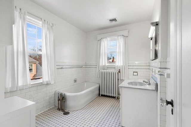 bathroom featuring radiator, tile patterned flooring, vanity, a tub, and tile walls