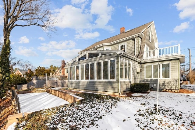 snow covered back of property featuring a balcony and a sunroom