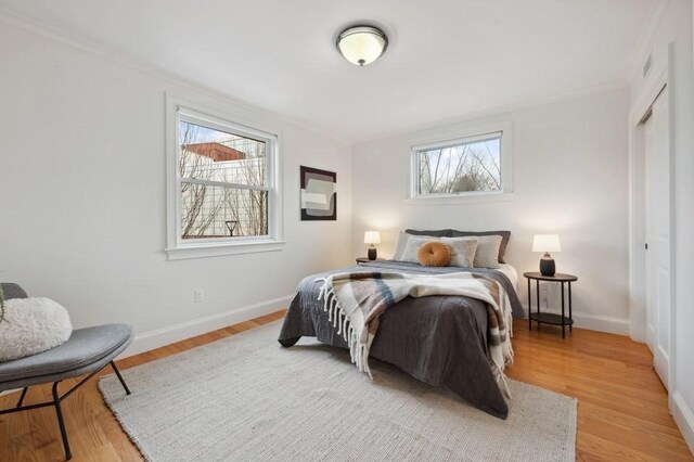 bedroom featuring light wood-style flooring, visible vents, baseboards, ornamental molding, and a closet