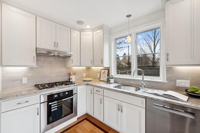 kitchen with pendant lighting, appliances with stainless steel finishes, white cabinetry, a sink, and under cabinet range hood