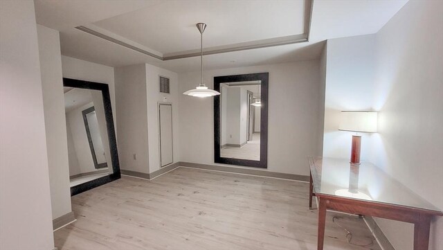 unfurnished dining area with baseboards, a tray ceiling, light wood-style flooring, and visible vents