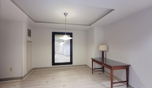 unfurnished dining area with baseboards, a tray ceiling, light wood-type flooring, and visible vents