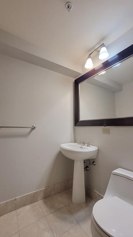 half bath featuring baseboards, tile patterned flooring, and toilet