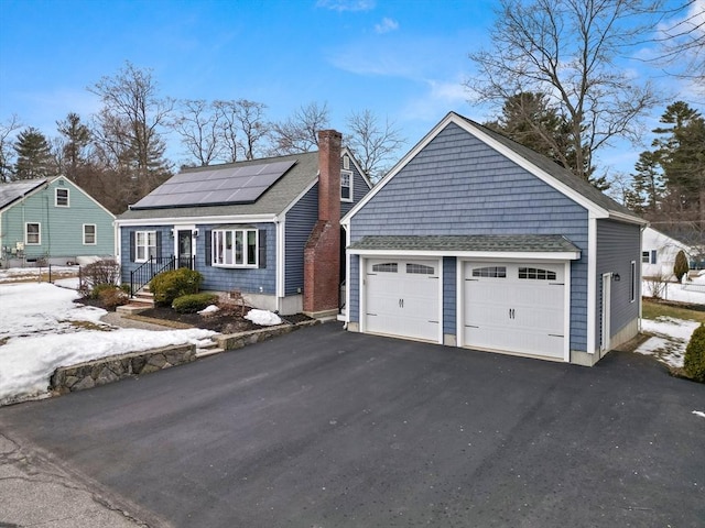 view of front facade featuring a garage, a shingled roof, a chimney, and roof mounted solar panels