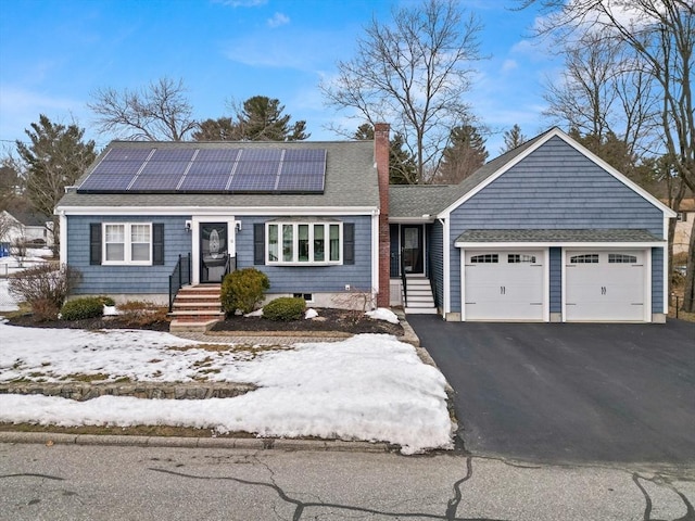 view of front of home with a chimney, a shingled roof, roof mounted solar panels, a garage, and driveway