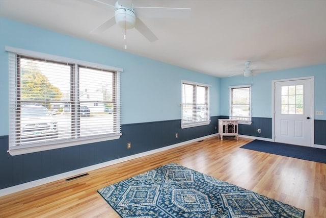 entrance foyer featuring ceiling fan, a wainscoted wall, visible vents, and wood finished floors