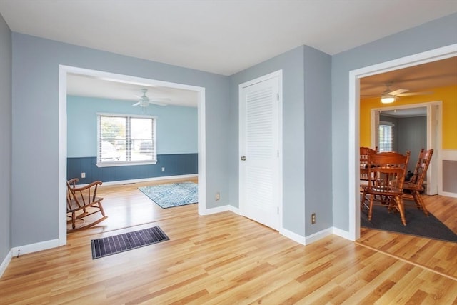 interior space with a ceiling fan, baseboards, wood finished floors, visible vents, and wainscoting