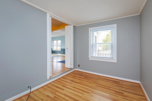 empty room with crown molding, wood finished floors, and baseboards