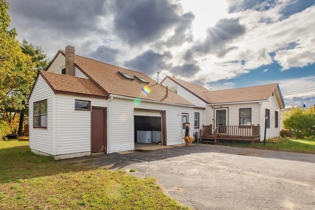 view of front of house featuring a wooden deck, a shingled roof, a front lawn, a garage, and aphalt driveway