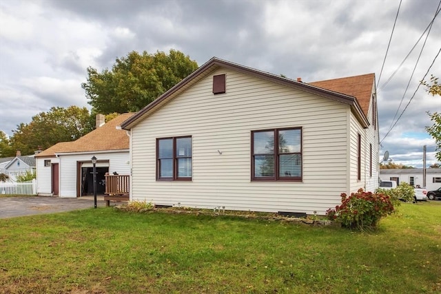 view of side of home with aphalt driveway, a lawn, an attached garage, and fence