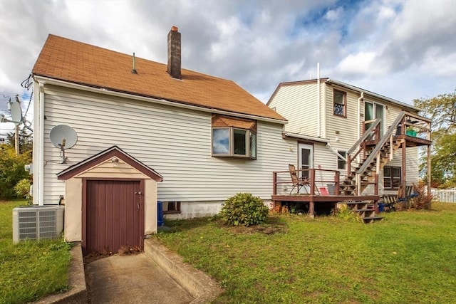 rear view of property featuring central air condition unit, a lawn, a deck, an outdoor structure, and a chimney