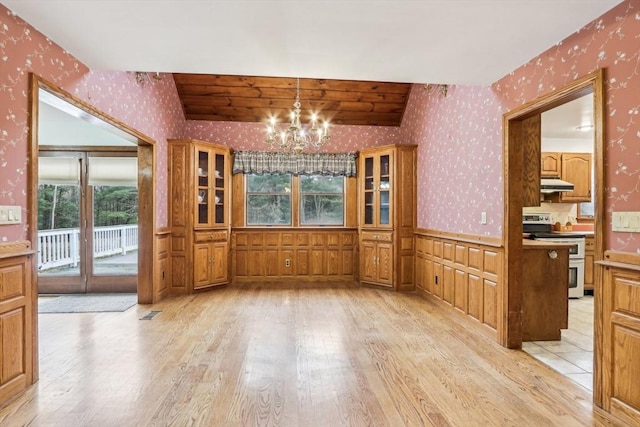 unfurnished dining area with light hardwood / wood-style floors, vaulted ceiling, and a notable chandelier