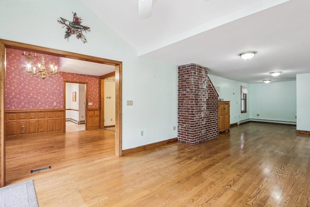 unfurnished living room featuring lofted ceiling, an inviting chandelier, wood-type flooring, and a baseboard heating unit