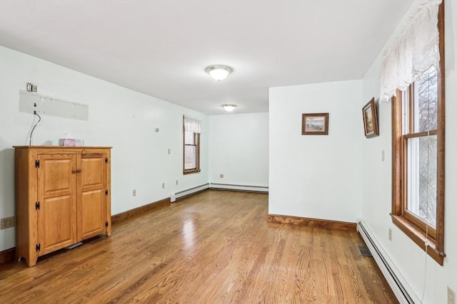 unfurnished room with hardwood / wood-style flooring, a wealth of natural light, and a baseboard heating unit