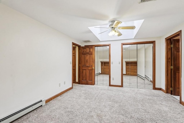 unfurnished bedroom featuring light carpet, a skylight, ceiling fan, a baseboard radiator, and multiple closets