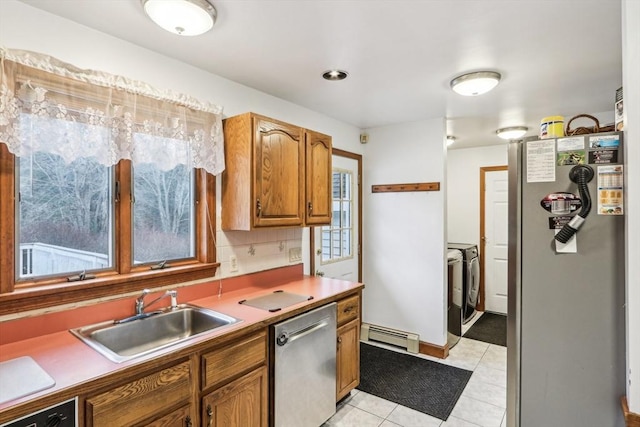 kitchen featuring sink, a baseboard radiator, washing machine and dryer, light tile patterned floors, and appliances with stainless steel finishes