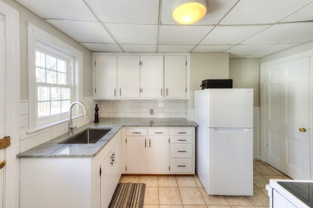 kitchen featuring sink, light tile patterned floors, white refrigerator, white cabinets, and backsplash