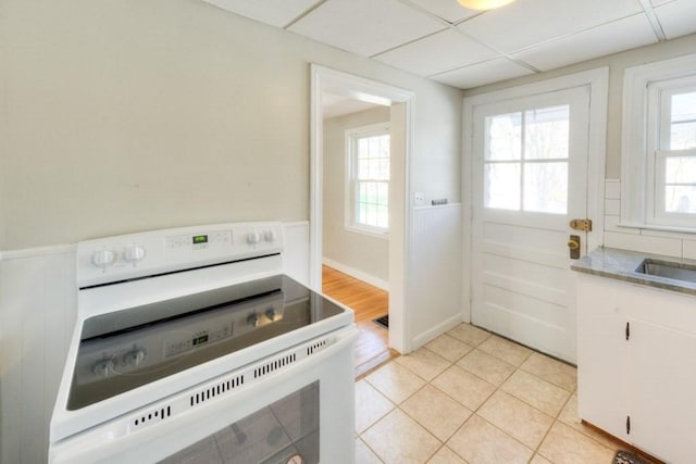 kitchen with electric stove, plenty of natural light, white cabinets, and a paneled ceiling