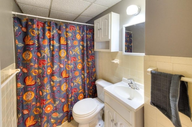 bathroom with a paneled ceiling, tile walls, vanity, curtained shower, and toilet