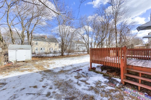 snowy yard with a wooden deck and a storage unit