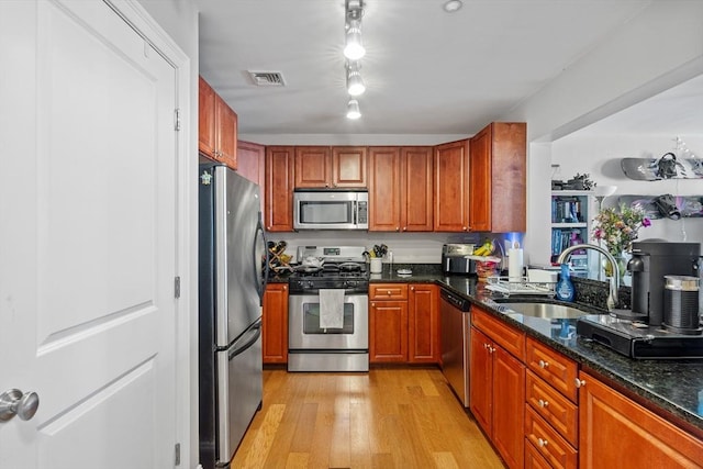 kitchen with appliances with stainless steel finishes, a sink, light wood-type flooring, dark stone counters, and brown cabinets