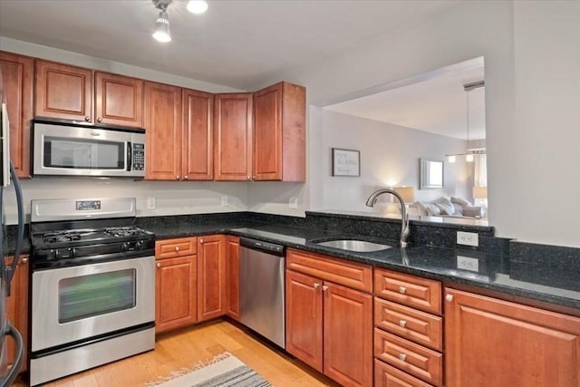 kitchen with appliances with stainless steel finishes, a sink, brown cabinetry, and dark stone counters