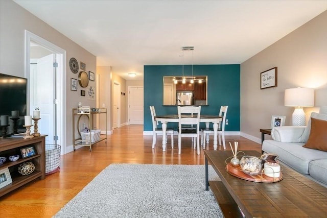 living room with light wood finished floors, a chandelier, and baseboards