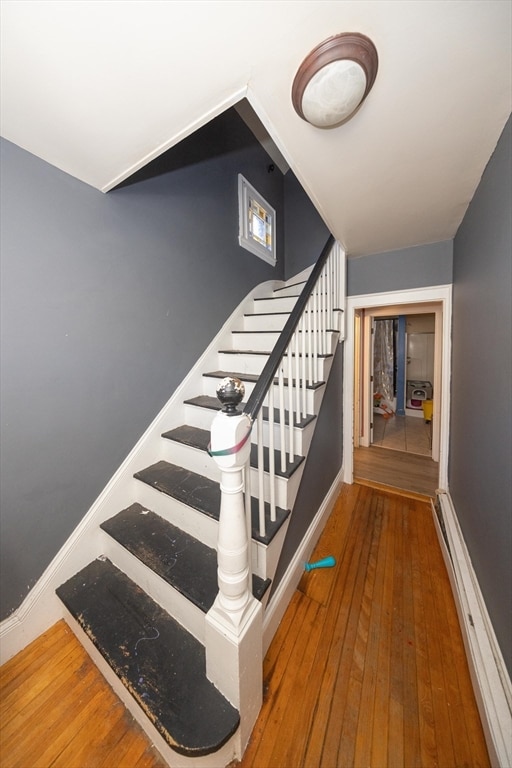 stairs with baseboard heating and wood-type flooring