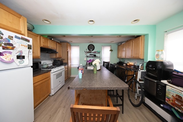 kitchen with light hardwood / wood-style flooring, decorative backsplash, and white appliances