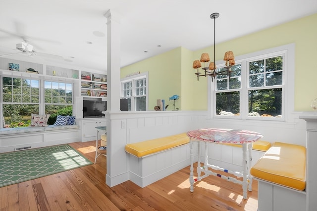 dining area with built in features, ceiling fan with notable chandelier, light wood-type flooring, and a wealth of natural light