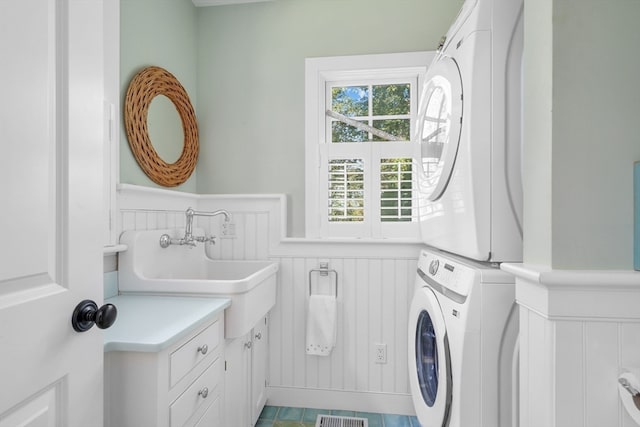 laundry room with tile patterned flooring, stacked washer and dryer, cabinets, and sink