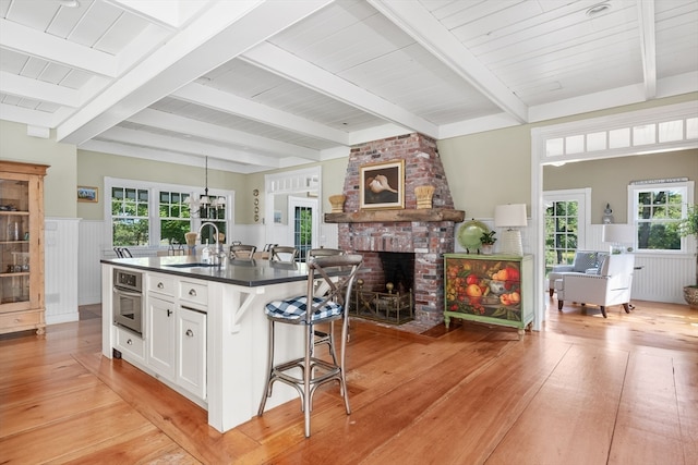 kitchen with light hardwood / wood-style flooring, a kitchen island with sink, white cabinetry, a kitchen breakfast bar, and stainless steel oven