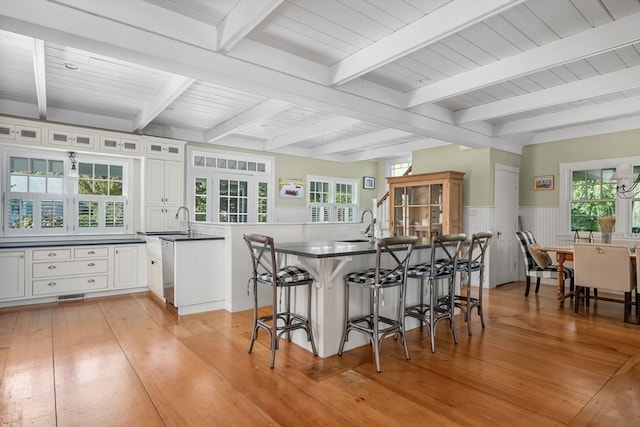 kitchen with beamed ceiling, a breakfast bar area, light hardwood / wood-style flooring, and white cabinets