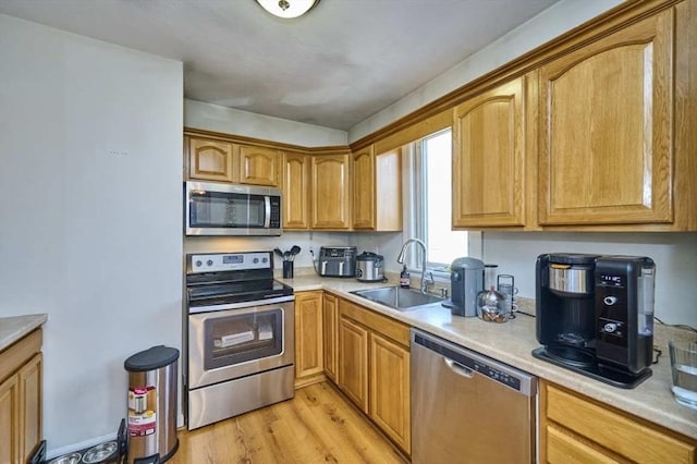 kitchen with stainless steel appliances, a sink, light countertops, and light wood-style floors