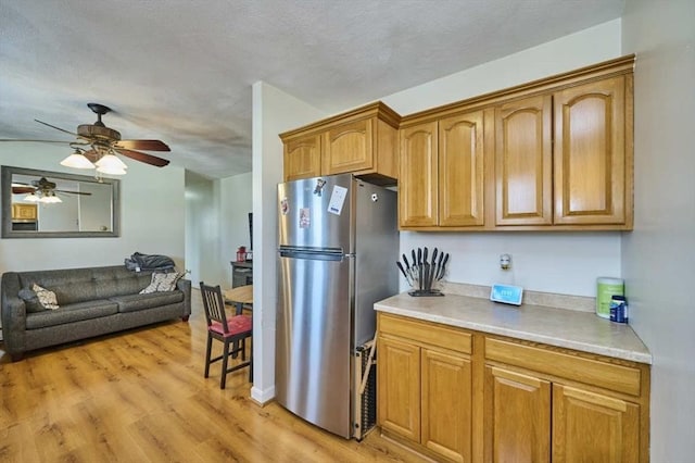 kitchen with light wood finished floors, brown cabinetry, open floor plan, freestanding refrigerator, and light countertops