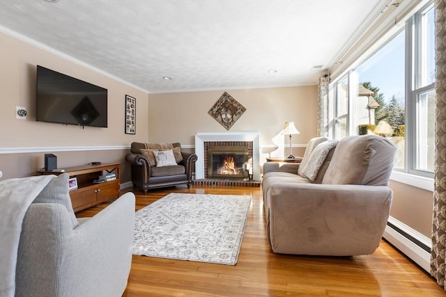 living room featuring crown molding, a fireplace, a baseboard radiator, and light wood-type flooring