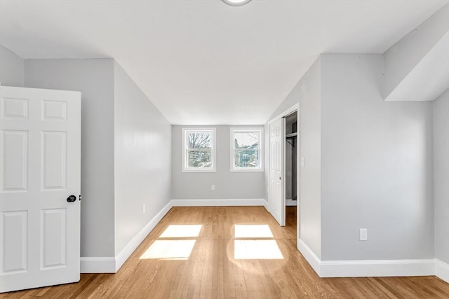 unfurnished bedroom with a closet, baseboards, lofted ceiling, and light wood finished floors