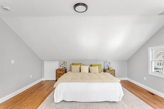 bedroom featuring lofted ceiling, light wood-style floors, visible vents, and baseboards