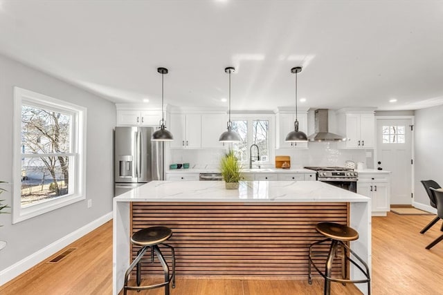 kitchen featuring visible vents, a kitchen island, stainless steel appliances, wall chimney range hood, and decorative backsplash