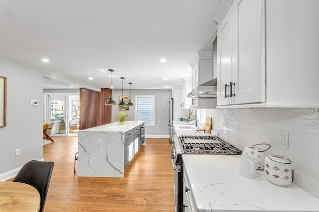 kitchen featuring stainless steel range with gas cooktop, light wood-type flooring, a kitchen island, white cabinets, and tasteful backsplash