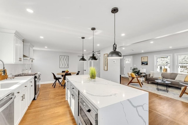 kitchen featuring a sink, stainless steel appliances, white cabinetry, light wood-type flooring, and a center island