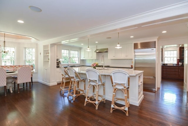 kitchen with crown molding, stainless steel built in fridge, wall chimney exhaust hood, and dark wood-type flooring