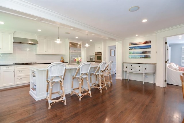 kitchen with decorative backsplash, dark wood-type flooring, wall chimney exhaust hood, white cabinetry, and appliances with stainless steel finishes