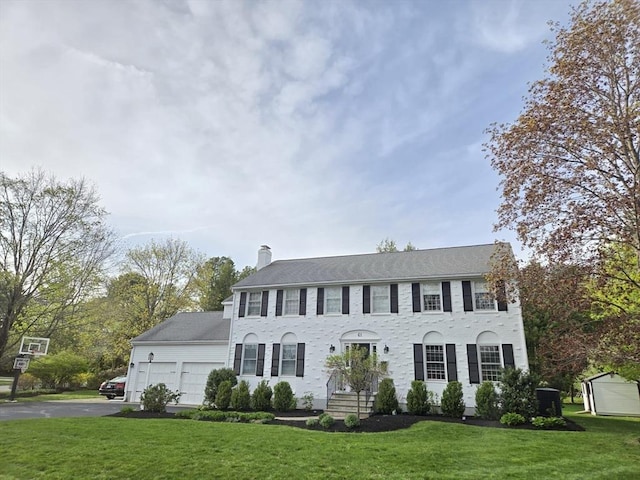 colonial-style house featuring an attached garage, driveway, a chimney, and a front yard