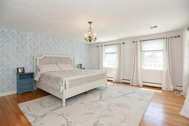 bedroom featuring visible vents, wood finished floors, a baseboard radiator, an inviting chandelier, and wallpapered walls